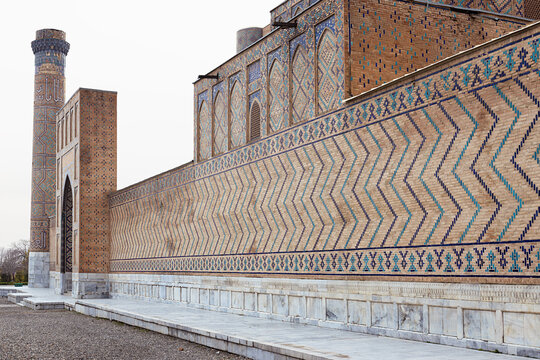 Bibi Khanum Mosque exterior wall with geometric brickwork and turquoise tilework in Samarkand. Detailed Islamic ornamentation and minaret under overcast sky, ideal for travel and heritage.