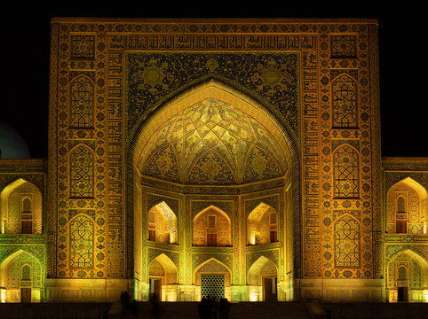 Illuminated Tilla-Kari madrasah facade at Registan Square in Samarkand with intricate tilework, grand iwan at night. Ideal for travel publications, cultural heritage materials, architecture features.