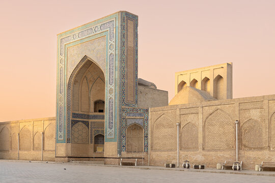 Kalyan Mosque entrance portal on Poi Kalyan Square in Bukhara at sunset. Ornate tilework and brickwork facade against a pastel pink sky, ideal for travel and cultural heritage publications.