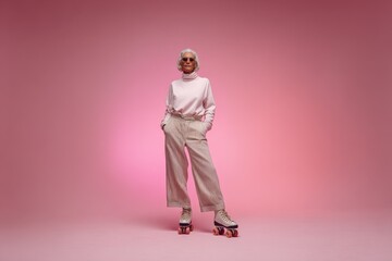 Fototapeta premium Elegant grandmother on retro roller skates in sporty trousers against a pink studio backdrop