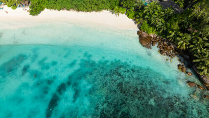 Obraz premium Turquoise lagoon with coral reefs meets a white sand beach surrounded by lush green vegetation. Seychelles, Mahe. Petite Anse.