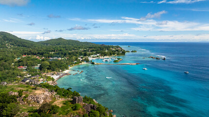 Turquoise water meets lush green coastline with boats anchored near the shore. Seychelles, La Digue. © Alex Traveler