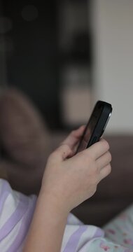 Vertical video. Close up little child girl using mobile phone at home. Daughter scrolling smartphone technology watching funny video in social media. The problem of addiction to gadgets.
