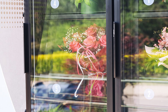 Flower bouquet inside vending machine closeup. Automated flower shop and self service florist concept. Fresh roses behind glass display background. Modern urban flower purchase service.