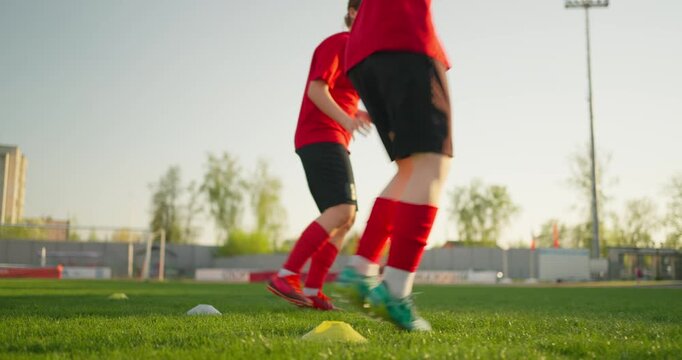 Young soccer players in red uniforms practicing footwork drills around cones on a sunny outdoor grass field during team training session