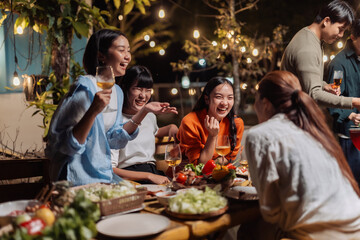 Happy asian friends gathering for an evening outdoor dinner party, sharing food and drinks, laughing and socializing © Crystal