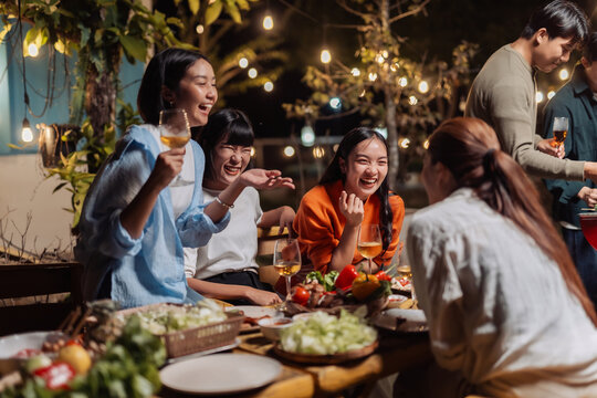 Happy asian friends gathering for an evening outdoor dinner party, sharing food and drinks, laughing and socializing