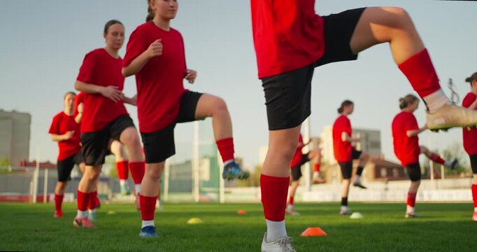 Youth soccer team in red uniforms performing speed and agility drills with cones on a sunny outdoor grass field during practice