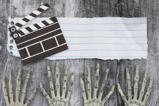 Two pairs of skeleton hands on with ripped paper and movie clapper on weathered wood
