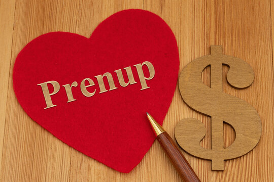 Prenup text on a red heart with a pen and a dollar sign on a wood desk
