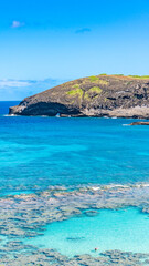 Obraz premium A high angle panoramic scenic landscape view of Hanauma Bay with an extensive shallow coral reef and turquoise ocean water under a blue sky in Hawaii