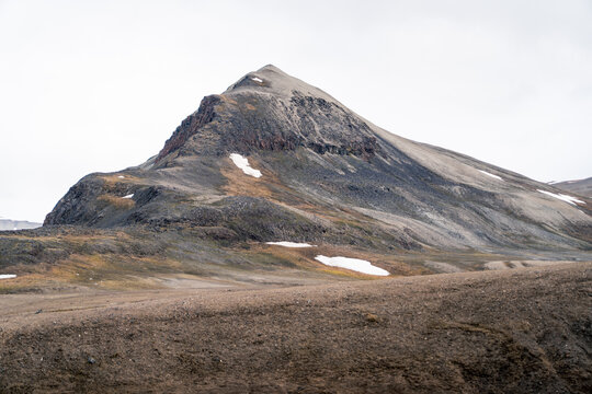 View of a rugged mountain peak with patches of snow and barren rocky terrain under an overcast sky in Svalbard and Jan Mayen.