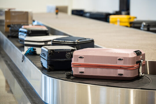 Many personal luggage transporting from airplane to arrival area in modern airport terminal, suitcases and bags lying on conveyor belt line, arrival zone with automatic carousel for passengers baggage