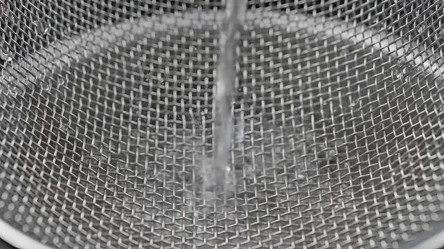 Closeup of water flowing through a fine metal mesh sieve.
