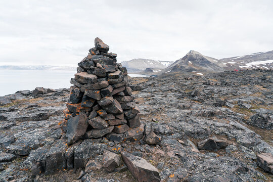 View of a stone cairn on a rocky plateau overlooking mountains and a fjord under a cloudy sky Svalbard and Jan Mayen.