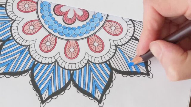 Female hand coloring an intricate geometric mandala ornament with a blue pencil. Creative art pattern stands on white paper. Meditation hobby concept