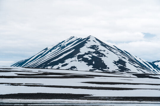 View of a snow-covered mountain peak under a cloudy sky with patches of snow on the ground Svalbard and Jan Mayen.
