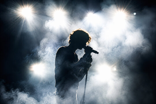 A musician performing on a dark stage illuminated by bright spotlights and surrounded by smoke.