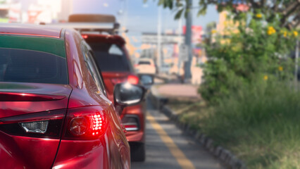 Vibrant red hatchback stands still in a gridlocked traffic lane during a bright day. The yellow lane markings and green roadside bushes frame the dense queue of modern city vehicles ahead. © thongchainak