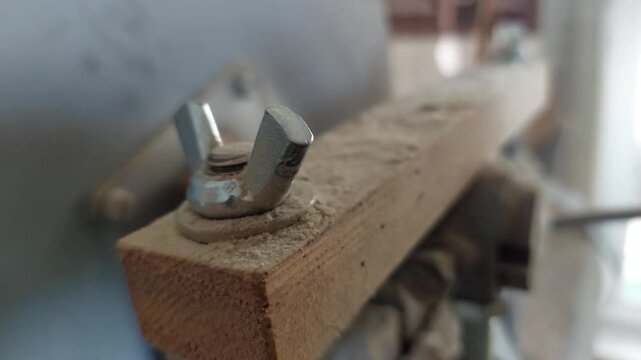 Close-up of a metal wing nut on a dusty wooden machine in a workshop