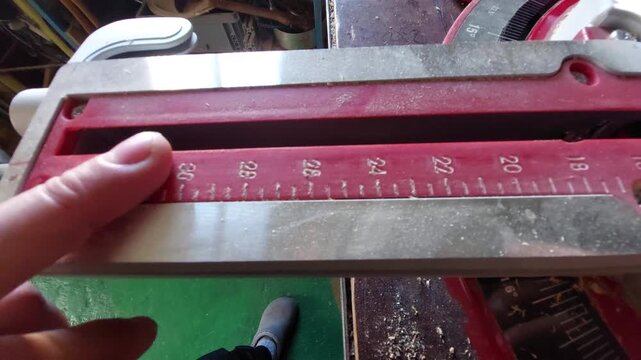 Finger pointing at the red measurement scale on a miter saw in a workshop