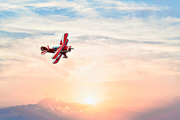 A red aerobatic biplane performing air shows against an orange sunset sky. Classic airplanes © Toni