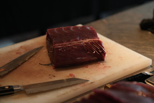 Fresh raw tuna steak on cutting board with knife, seafood preparation, close-up traditional market food photography