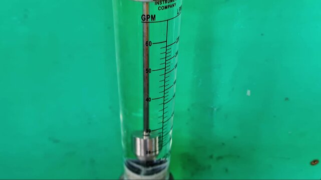 Industrial glass tube rotameter flow meter for liquid measurement against a green background.
