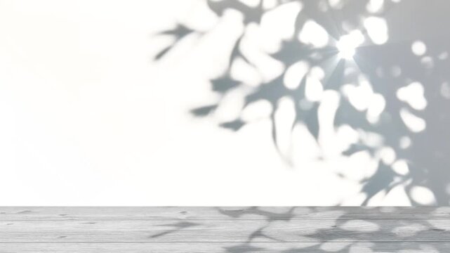 blurred shadow of leaves with sunlight isolated on wooden table and white wall background, copy space in abstract nature, slow motion shades of gray texture template 