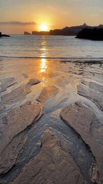 Vertical 4K footage of flowing seawater across reflective wet sand with bronze tones during calm Atlantic sunrise. Marble-like beach textures and gentle ocean motion in soft summer morning light.