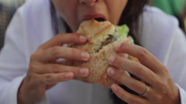Woman eating burger closeup at outdoor cafe, hands holding gourmet sandwich and taking bite, casual dining lifestyle, comfort food craving, authentic social connection