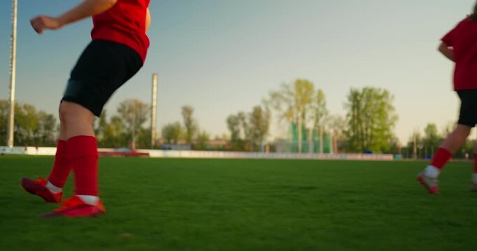 Low angle view of youth soccer players in red uniforms dribbling and sprinting with a ball across a green outdoor field during practice