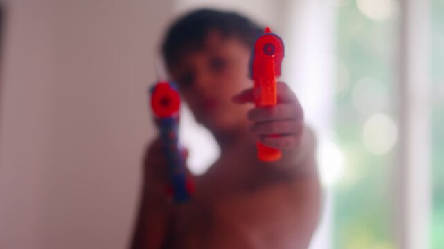 Young boy pointing colorful toy blasters toward camera during imaginative indoor play capturing pretend action, childhood fantasy and energetic carefree entertainment at home