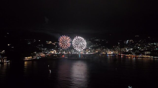 A dynamic display of continuous fireworks lighting up the night sky over Atami Bay. This high-angle shot captures the colorful reflections on the water, representing traditional Japanese summer celebr