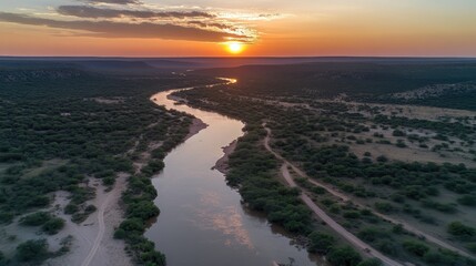 Fototapeta premium Warm sunset glow over a winding river and arid landscape, capturing serene natural beauty at dusk.