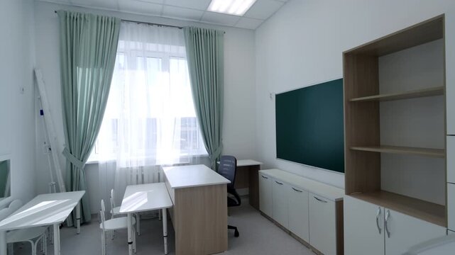 Large chalkboard surrounded with multiple cabinets fills well lit classroom. Modest workspace creates calm and productive mood for staff