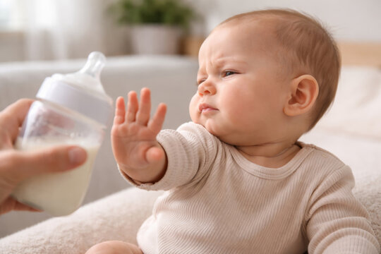 Baby rejecting bottle while sitting on a cozy surface