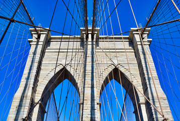 Obraz premium Brooklyn Bridge granite tower with gothic arches and suspension cables seen from walkway against vivid blue sky, close-up architectural detail, New York City