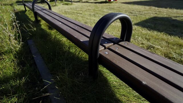 Dark wooden planks form long sitting bench outdoors. Simple durable design fits perfectly into natural park landscape. Space for relaxation