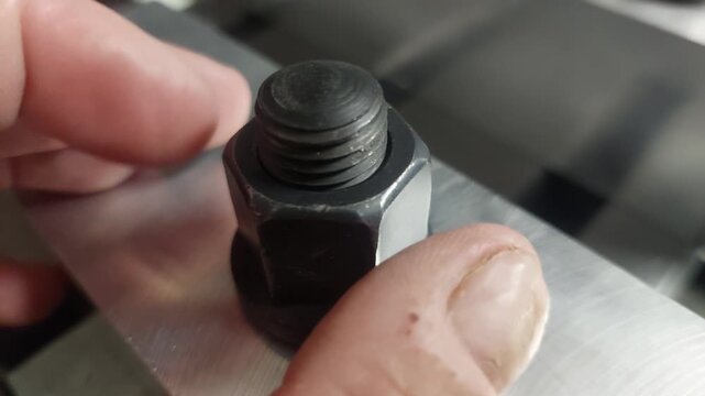 Close-up of a worker tightening a heavy-duty black steel nut on a clamping bolt