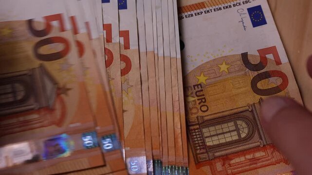 Several fifty euro banknotes placed on a smooth wooden table, showcasing currency details and textures. Warm tones highlight the contrast between paper money and natural wood grain patterns.