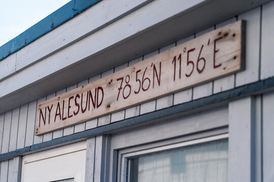 Ny-Alesund, Svalbard and Jan Mayen - 17 June 2025: View of a wooden sign displaying the name and geographic coordinates of the settlement on a white building.