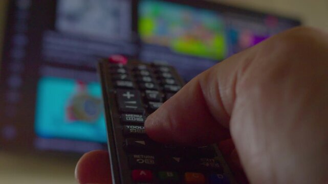 First-person view of a hand using a remote control to change channels and then turn off a modern TV, close-up, shallow depth of field