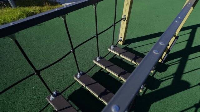 Rope ladder hangs from sturdy wooden playground frame. Challenging climbing equipment helps children develop physical strength and balance