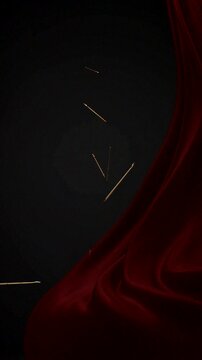 Golden needles float beside rich red velvet fabric against a dramatic dark background in abstract composition.