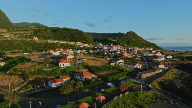 Aerial drone panoramic view of a coastal village with traditional white houses and terracotta roofs sprawling across green slopes by the Atlantic Ocean, Flores Island, Azores.