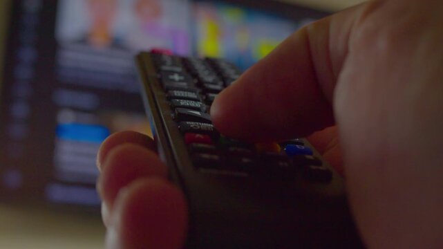 A man's hand controls a modern TV hanging on the wall with a remote control. Close-up. Shallow depth of field. First-person view.