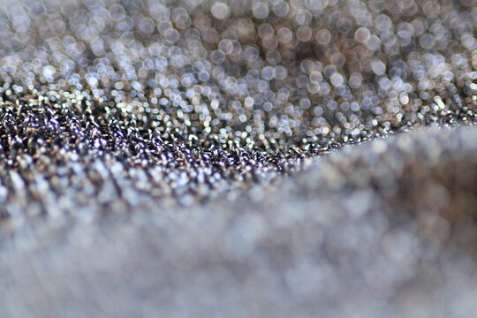 Macro shot of shiny polyester fabric texture with sparkling glitter threads and beautiful festive bokeh.