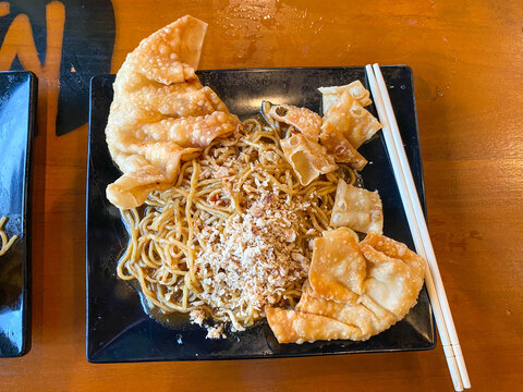 Top down view of spicy Indonesian fried noodles served with crispy fried wontons and minced chicken on a black plate