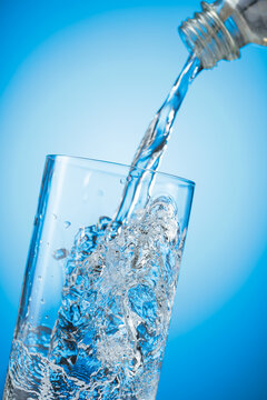 Clear drinking carbonated water pouring into a tall glass from a transparent plastic bottle.